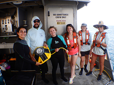 Sanctuary staff in dive gear or life vests holding the yellow sofar buoy and cable on the deck of R/V MANTA.