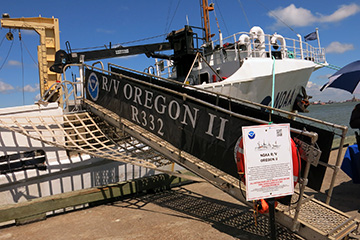 A small sign with an outline of the ship and a brief description stands next to the gangway leading up to the ship's deck.