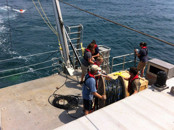 Students with a large reel of cables on the back deck of R/V MANTA