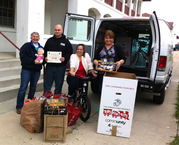 Four people posing with toys collected and ready to be loaded into a van for Toys for Tots