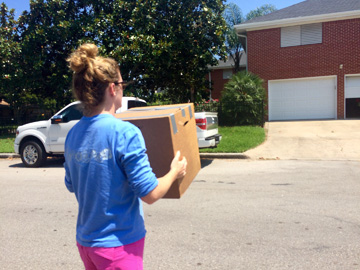 Woman carrying a cardboard box across the street to a house