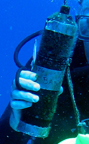 A closeup up view of an acoustic receiver in the hand of a diver.  The receiver is about the size and shape of a 1 liter bottle.