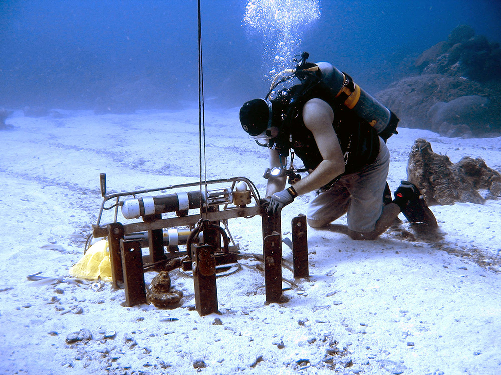 A diver kneeling next to equipment on the sea floor in a sand patch