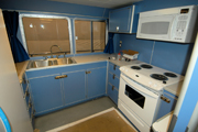 The kitchen area of the vessel with a stainless steel double sink, white stove and white microwave oven visible.  All of the cabinets are light blue.