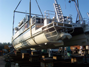Stern view of an 83-foot boat being hoisted by crane and set down on the rails that will be used to launch the boat into the water for the first time.