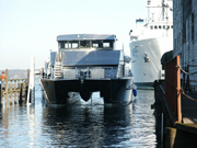 Bow view of the R/V Manta floating in the water for the first time.  Piers partially visible on either side of the photo.  Large white ship visible in background.