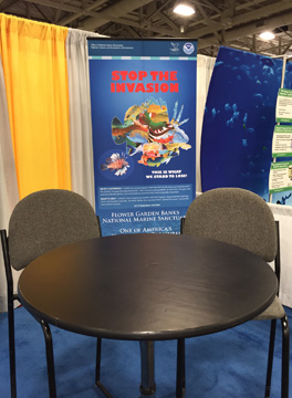 A small table with 2 chairs in front of a Stop the Invasioni banner with the outline of a lionfish filled with images of other fish lionfish have been eating