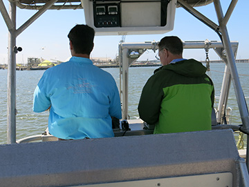 Looking at two men with their backs to the camera as they look at the stern controls of R/V MANTA on the upper deck..