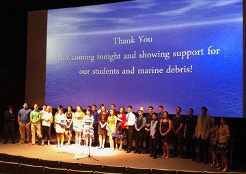 A group of students and their teacher standing as a group in front of a movie theater screen.