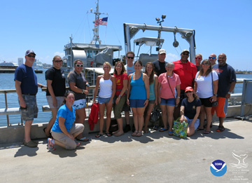 Group of people posing for a photo on the top deck of a dive boat as it returns to shore.