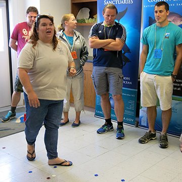 Jennifer standing in the middle of a room with teachers circled around her as she explains a game