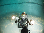 Plush bear toy in a sealed acrylic container modeled to look like a submersible.  In front of the submersible is an underwater camera set up with lights on either side.