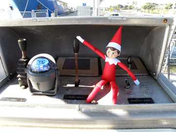 Elf doll sitting at the winch controls of R/V MANTA with his hand on the Trawl Winch control.