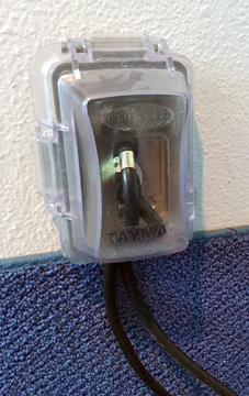 Plastic cover over electrical outlet with cords running out the bottom