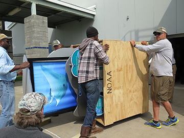 Four men moving a crated exhibit piece on its side