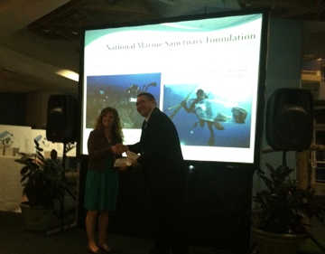 Michelle being handed an enveloped in front of a screen that says National Marine Sanctuary Foundation