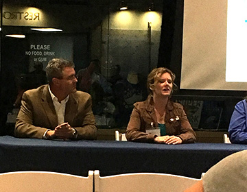 A man (left) and a woman (right) seated at a table in front of an audience as part of a panel discussion.