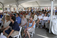A side view of all the guests seated under the catering tents facing the speakers' dais to the left.
