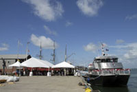 A view of Pier 21 with the Manta alongside, showing the large white tents where guests are seated for the ceremony.  Tents are to the left, boat to the right.