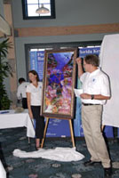Emma Hickerson and G.P. Schmahl standing on either side of a large, colorful painting of marine life in the Flower Garden Banks.  The vertically oriented painting is displayed on an easel.