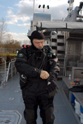 Dan, in full dry suit and hood, putting on his dive gloves while standing on the main deck