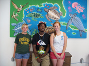 Three people and a stuffed bear pose in  front of a painting showing sea life of the Gulf of Mexico.