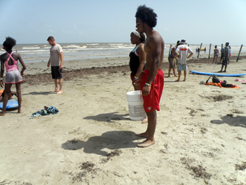 Students standing on beach holding a bucket for collecting trash.