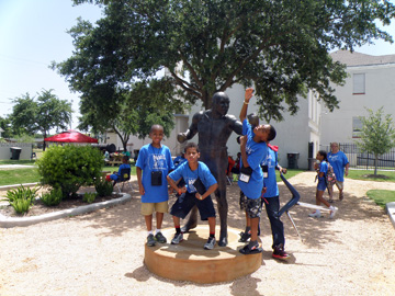 Three students pose with a Jack Johnson statue in a park.