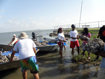 Students loading bags of oyster shell onto two small boats.