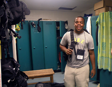 A student in a locker room area with dive gear slung over one shoulder.