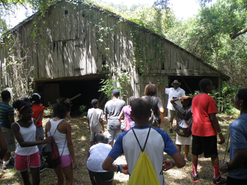 Students standing outside an old wooden barn that looks like it is about to collapse.