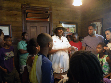 Sam Collins III talkikng to a group of students inside one of the wood-paneled rooms of an historic house.
