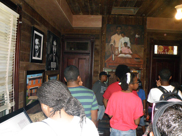 A group of people inside a wood paneled room decorated with art representing African American history.