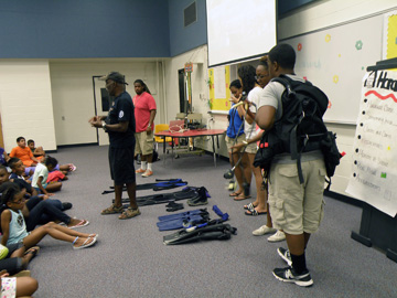 Students showing scuba equipment to other students seated on the floor in front of them.