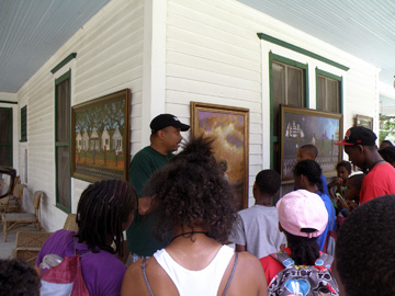 A gentleman explaining paintings displayed on the front porch of an historic house.