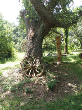 An old wooden wagon wheel leaning up against the trunk of a tree.
