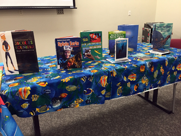 A table covered with a colorful fish fabric displays kids books about oceans and ocean heroes.