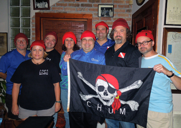 A group of dive club members wearing red watch caps and holding a pirate flag