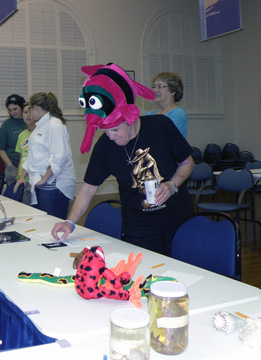 A woman wearing a purple a black fish hat while looking at something on a table