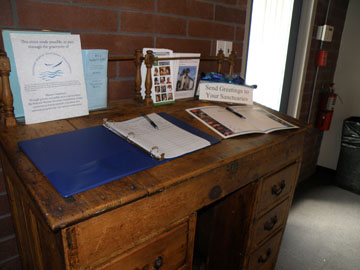 Wooden captain's desk with a sign-in log and an anniversary card for people to sign.
