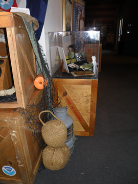 An old lantern and some rope floats sitting on the floor next to a display case.