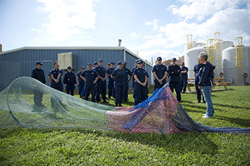 Group of Coast Guard staff, in uniform, standing behind a shrimp net with TED installed, on the lawn by the turtle barn.
Kelly Drinnen is on the right explaining how the TED works.