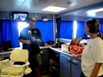 Two people standing in the dry lab of R/V Manta adjusting equipment.