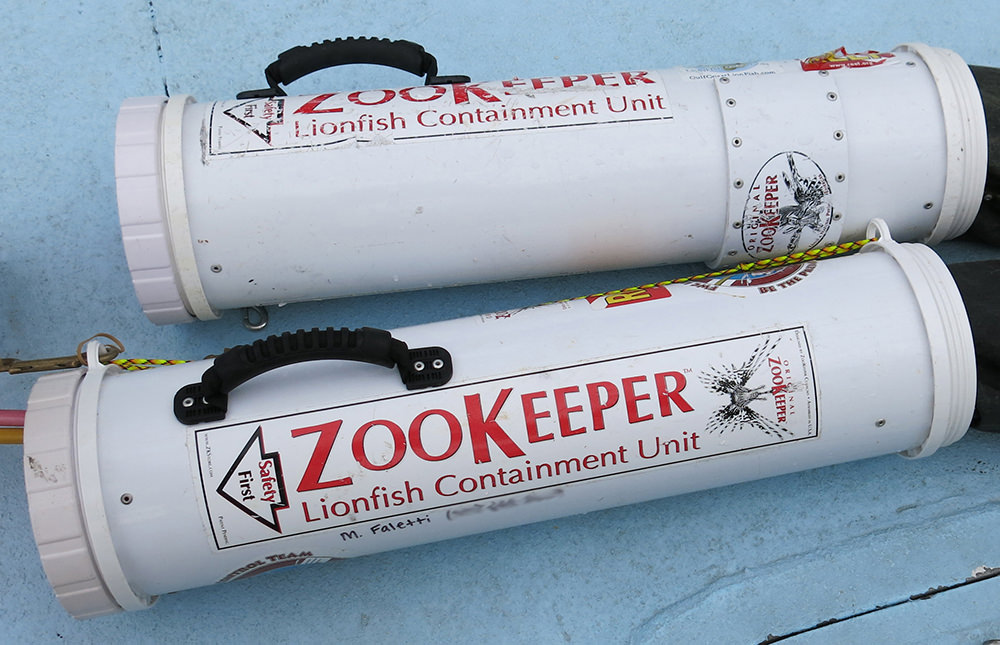 A pair of modified white pvc tubes called ZooKeeper Lionfish Containment Units lying on the deck of a boat