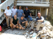 Seven men take a break alongside/on a pile of drywall they helped remove from a house