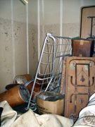 Small barrels, equipment and tables inside a water-damaged storage unit.  The flood line is visible six feet up the wall.