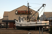 A bayside restaurant with a large shrimp boat sitting upright in the parking lot out front