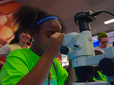 A student in a bright green shirt looking into a microscope