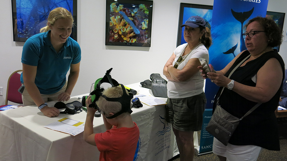 A woman from Moody Gardens helping a young boy try on a full face dive mask as two women watch nearby.