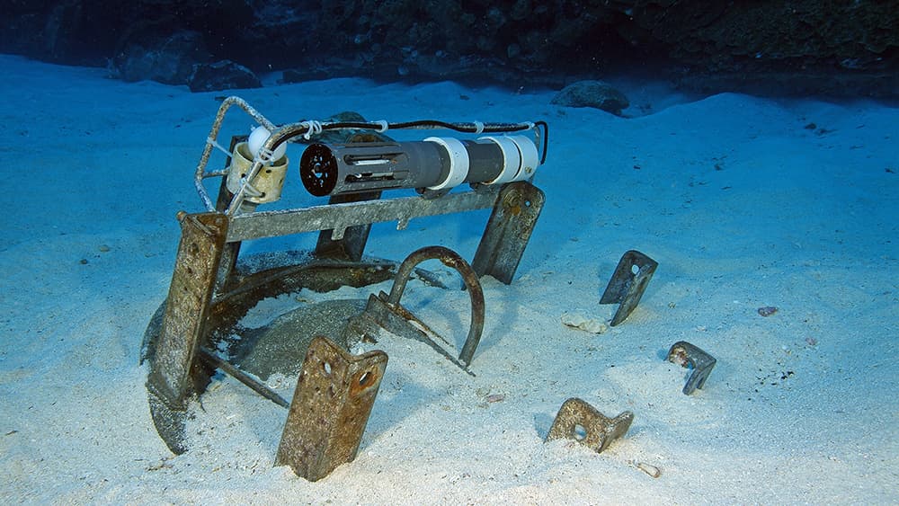 Scientific instruments partially buried in sand near the reef.